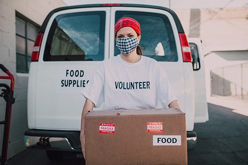 Volunteer wearing face mask holding a carton box with food label and most likely food