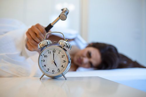 A woman uses a hammer to snooze her alarm clock after losing a precious hour of sleep to Daylight Savings Time