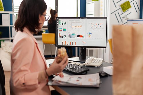 Businesswoman analyzing the latest market trends as she enjoys a tasty sandwich, likely with extra pickles and a variety of savory sauces 