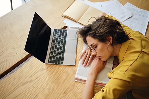 A student asleep on a textbook at their laptop