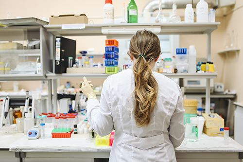 Rubber gloved Pharmacy Assistant in a lab surrounded by tools of her trade