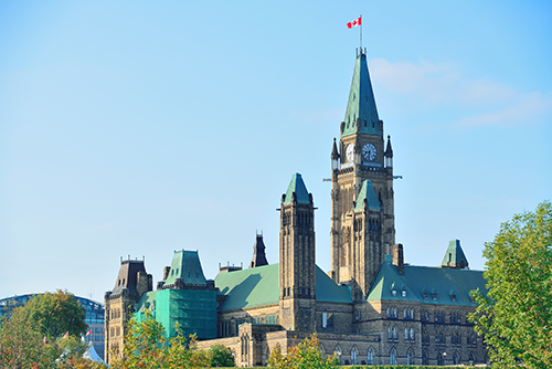 The majestic Canadian Parliament Hill Building in Ottawa with the Canadian flag waving proudly in the wind