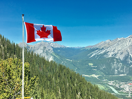 Canadian flag blowing in the wind overlooking a scenic valley in the Rockies