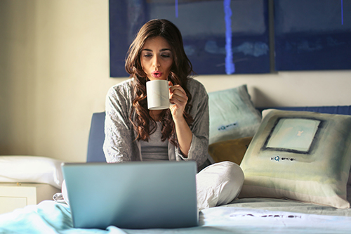 Lady working from home from the comfort of her bed sipping morning coffee