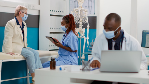 A young black physician assistant charts an elderly woman's vitals