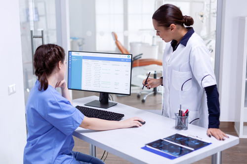 A nurse and a medical office assistant look over a patients chart on a computer