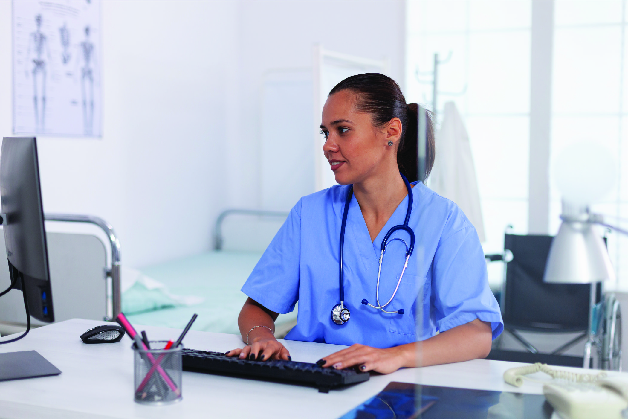 A young woman in blue scrubs charts a patients dental records as a part of her medical office admin duties